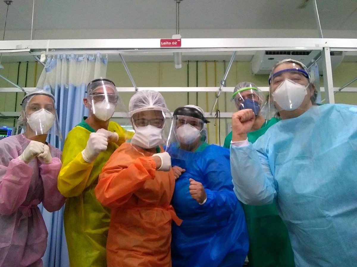 Equipe do plantão com aventais coloridos e protetores faciais, punhos erguidos