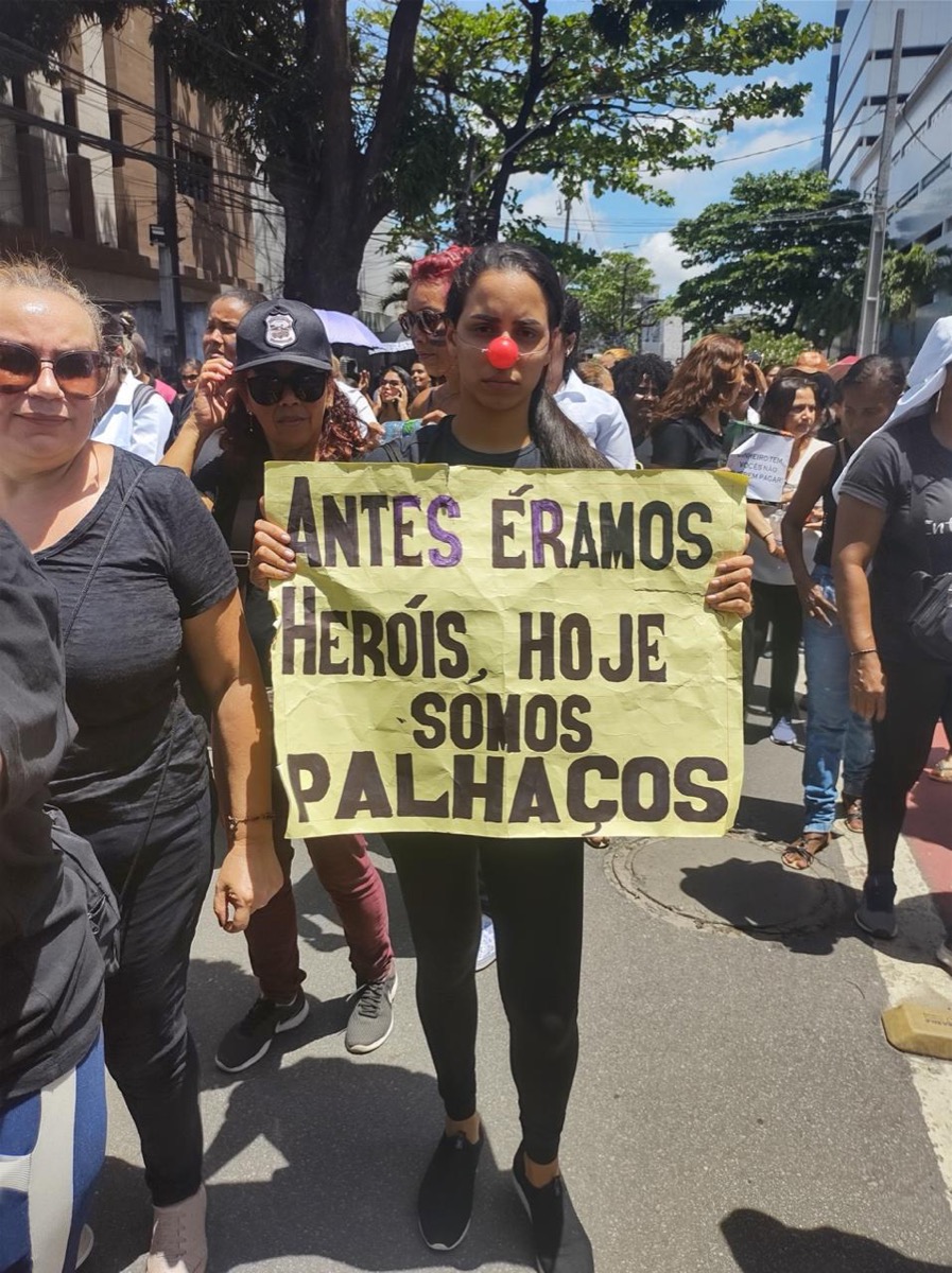 Camila Cardoso de nariz de palhaço segura cartaz em protesto da enfermagem