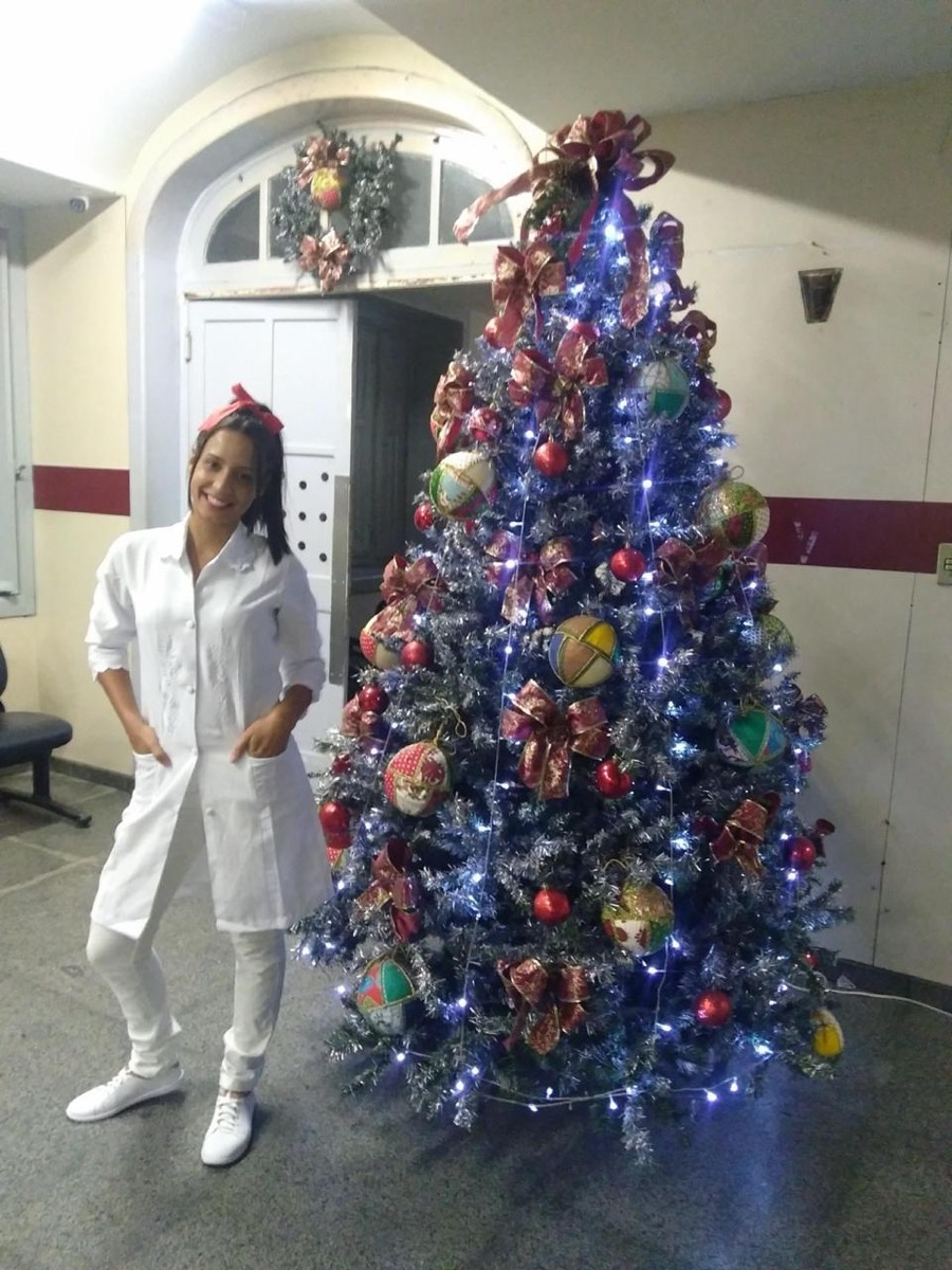 Camila Cardoso de jaleco branco ao lado da árvore de Natal do hospital