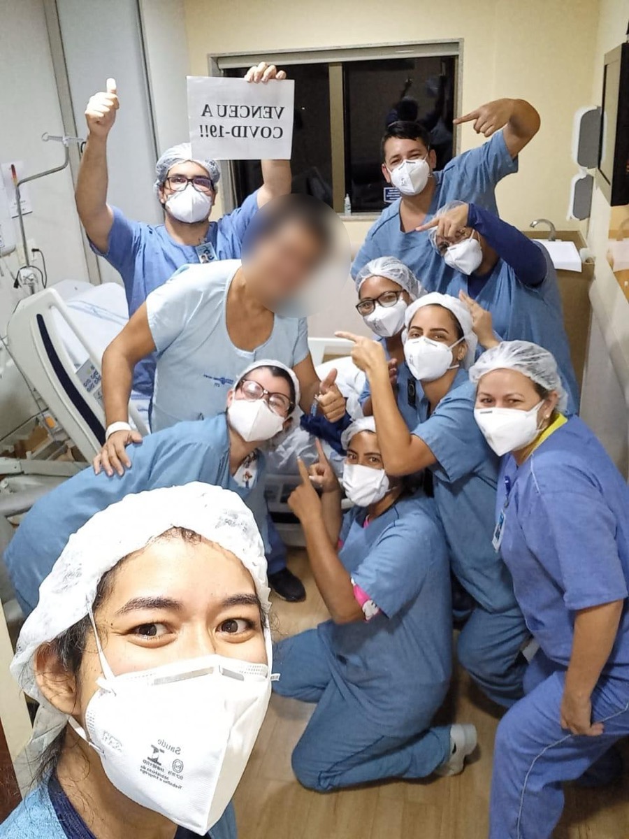 Equipe comemora a alta de um paciente que venceu a COVID-19; o rosto do paciente está borrado para preservar sua identidade